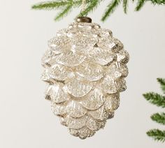 a glass pine cone ornament hanging from a christmas tree with green leaves and needles