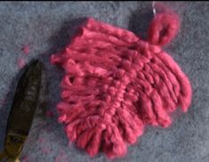 a pair of scissors are next to a pink piece of yarn on the ground,