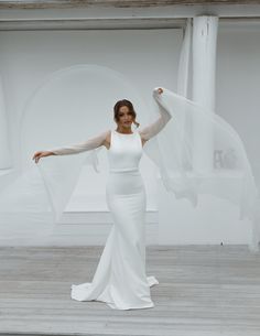 a woman in a white dress is posing with her arms spread out and she is wearing a veil