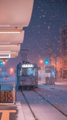 a train traveling down tracks next to a loading platform in the snow with traffic lights on