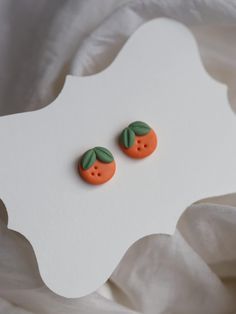 two oranges with green leaves on them are sitting on a white sheet and one is in the shape of a button