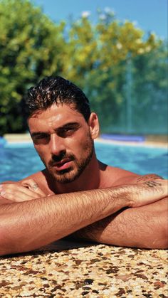 a man with his arms crossed leaning on the edge of a swimming pool