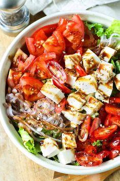 a salad with tofu, tomatoes and onions in a white bowl on a wooden table