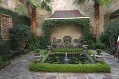 a courtyard with a fountain and seating area surrounded by greenery, palm trees and chairs