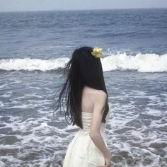 a woman standing in the ocean with her back to the camera, facing the water