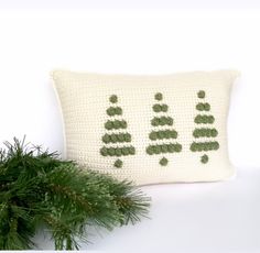 a crocheted pillow sitting next to a pine tree