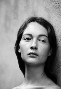 a black and white photo of a woman leaning against a wall with her eyes closed