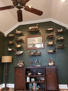 a living room filled with lots of shelves and birds on top of the wall next to a ceiling fan