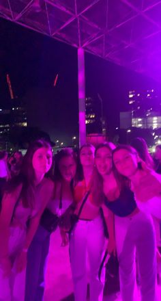 some girls are posing for the camera in front of purple lights