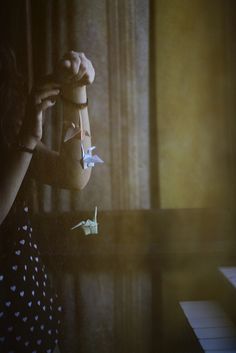 a woman standing in front of a window with paper birds hanging from her hands and the light shining on her face