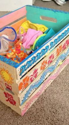 a wooden box filled with lots of colorful clothing and glasses on top of carpeted floor