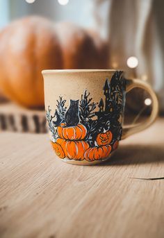 a coffee cup decorated with pumpkins on a wooden table next to some other items