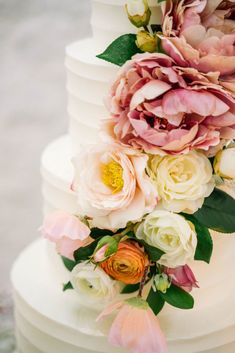 a white wedding cake with pink and yellow flowers on the top tier, along with greenery