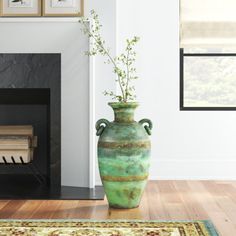 a green vase sitting on top of a hard wood floor next to a fire place