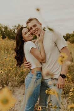 a man and woman are hugging in the middle of a field with wildflowers