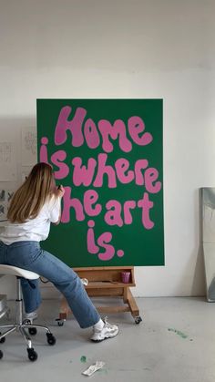 a woman sitting on a chair in front of a green sign that says home is where the art is