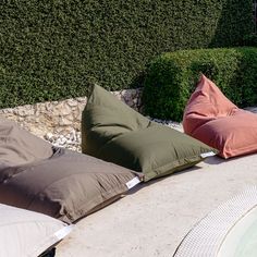 three pillows sitting next to each other on top of a stone floor near a pool