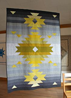 a quilt hanging from the ceiling in a room with wooden flooring and walls painted blue, yellow and gray