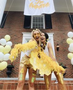 two women in gold and white costumes posing for the camera with balloons around them,