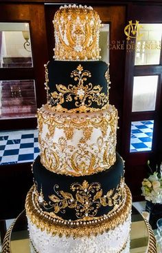 a three tiered cake with gold and black decorations on it's side, sitting on a table