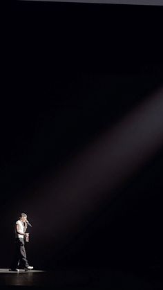 a man standing on top of a stage with a microphone in his hand and light coming from behind him