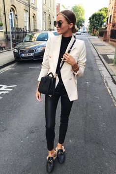 a woman is walking down the street wearing black pants and a white blazer jacket