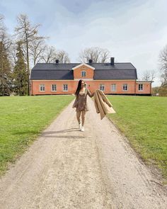 a woman walking down a dirt road with her arms outstretched in front of a house