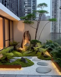 a garden with rocks, grass and trees in front of tall buildings at night time