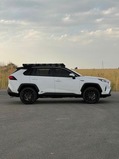 a white toyota rav parked in a parking lot next to tall grass and clouds