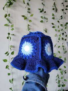 a blue crocheted hat with white flowers on the front and side, hanging from a vine