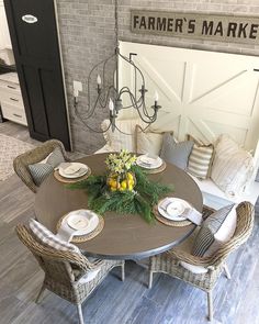 a dining room table set with place settings and flowers on the center piece, surrounded by wicker chairs