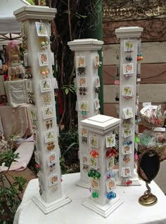 three white pedestals with jewelry on them sitting on top of a cloth covered table