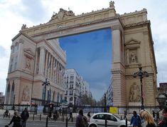 people walking on the sidewalk in front of an old building with a giant mirror reflecting it's facade