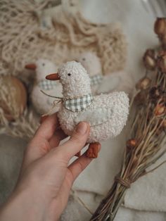 a person holding a small white stuffed animal next to some dried flowers and other decorations