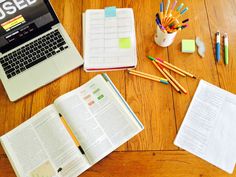 an open laptop computer sitting on top of a wooden table next to books and pencils