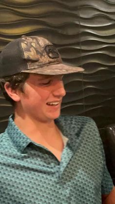 a man wearing a hat sitting in front of a wall with wavy waves on it