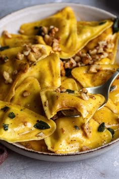 a white plate topped with ravioli covered in cheese and walnuts next to a fork