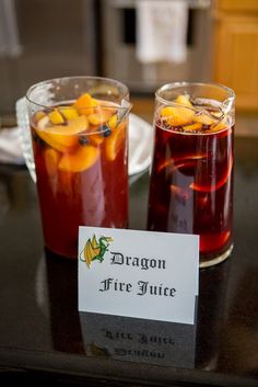 two glasses filled with liquid sitting on top of a table next to a sign that says dragon fire juice