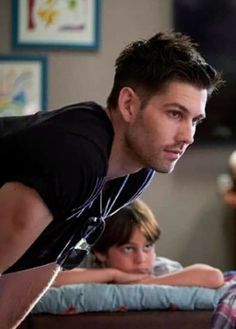 a man standing in front of a bed next to another person laying on the floor