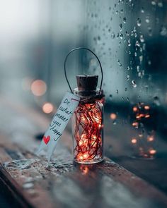 a jar filled with red string lights sitting on top of a wooden table next to a window