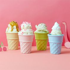 four ice cream cones with sprinkles and toppings in them on a pink background