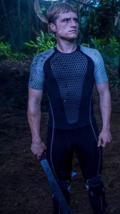 a man in a wet suit holding a knife and looking off into the distance with trees behind him