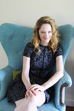 a woman sitting in a blue chair with her legs crossed on the armrests