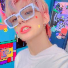 a person with pink hair and glasses on posing for a photo in front of a colorful background