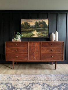 a painting on the wall above a dresser in a room with wood paneling and black walls