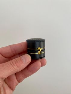 a small black and gold ring in the palm of someone's hand with white background