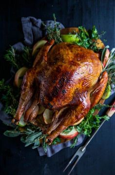 a roasted turkey on a platter with apples and herbs for garnishes