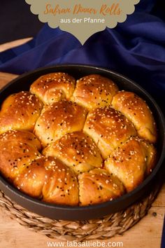 a pan filled with bread rolls on top of a wooden cutting board next to a blue cloth