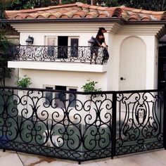 a woman standing on the balcony of a house next to a black wrought iron fence