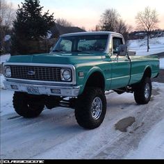 a green truck parked on the side of a snow covered road